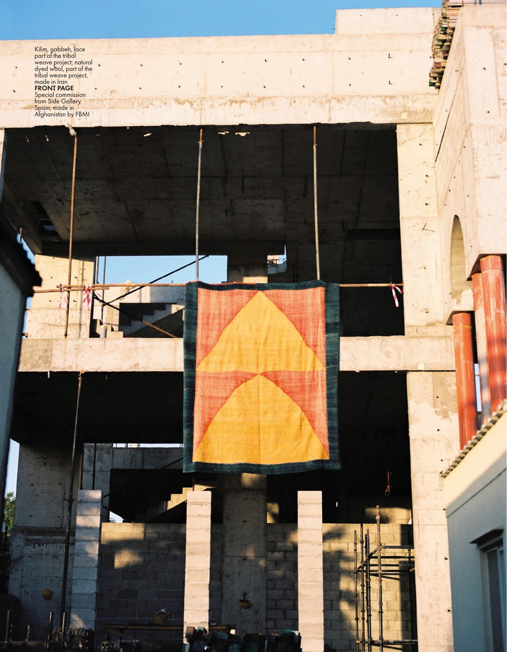 An orange and yellow triangle kilim from the Tribal Weave Project, hung from a pole inside an unfinished concrete building