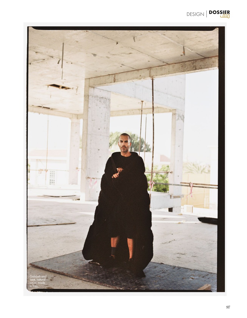 Taher Asad-Bakhtiari wrapped head to foot in a black gabbeh and lace piece, standing in a bare concrete interior